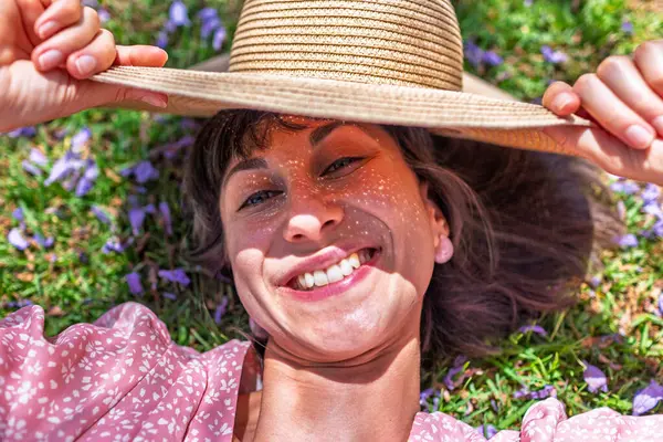 Yeşil çimlerin üzerinde yatan genç bir kadın. Yaz havası. Kız dışarıda vakit geçiriyor. Doğanın tadını çıkar. Üst Manzara. Sağlıklı gülümseyen kız baharda çimlerde.