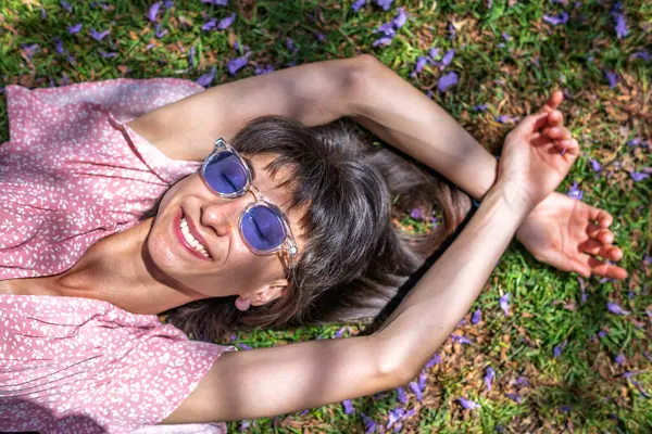 Yeşil çimlerin üzerinde yatan genç bir kadın. Yaz havası. Kız dışarıda vakit geçiriyor. Doğanın tadını çıkar. Üst Manzara. Sağlıklı gülümseyen kız baharda çimlerde.