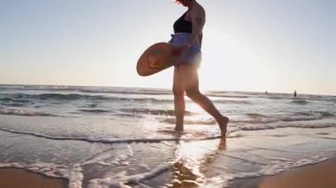 Altın gün batımında plajda yürüyen iri yarı bir kadının yan görüntüsü. Yaz tatilindeki kadın turist. Yaz havası. Sahildeki kız..