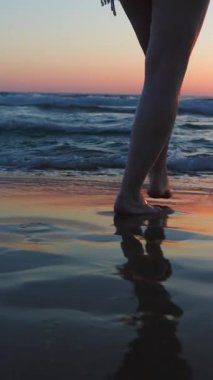 Dikey çekim. Genç ve iri yarı bir kadının bacaklarının yakın çekimi. Deniz kenarında kumsalda yalınayak yürümek. Yaz yaşam tarzı. Seyahat