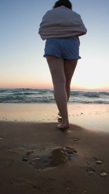 Dikey çekim. Genç ve iri yarı bir kadının bacaklarının yakın çekimi. Deniz kenarında kumsalda yalınayak yürümek. Yaz yaşam tarzı. Seyahat