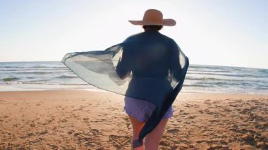 Ayrıca altın gün batımında plajda yürüyen şapkalı bir kadın. Yaz tatilindeki turist. Yaz havası. Sahildeki kız..