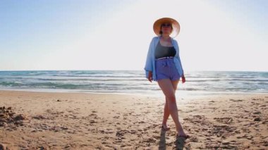 Artı, altın gün batımında plajda duran şapkalı kadın. Yaz tatilindeki kadın turist, yaz havası. # Kız #