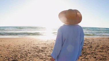 Artı, altın gün batımında plajda duran şapkalı kadın. Yaz tatilindeki kadın turist, yaz havası. # Kız #
