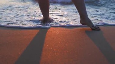 Sahilde çıplak ayaklı bir kadın. Deniz suyunda bacaklara ve ayaklara yakın çekim. Seyahat ve turizm, yaz havası konsepti.
