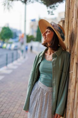 Genç bir esmer şehirde dururken mutlu bir şekilde gülümsüyor. Gömlekli, etekli ve şapkalı şık bir kız avlunun yanında duruyor. Yaz Portresi