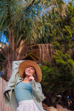 Güzel, gezgin, esmer bir kadının yakın plan portresi. Şapkalı, şık yaz kıyafetleri giyiyor. Yaz tatili boyunca sahilde gülümseyen neşeli genç bir kadın. Mutlu kız.