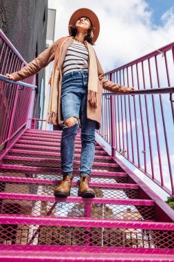 Şapkalı şık bir kız. Kendine güvenen bir kız merdivenlerden çıkar. Genç kız şehirde yürüyüş yapıyor. Moda tarzı.