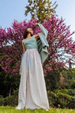 Genç kız şehirde mutlu bir şekilde duruyor. Şık yaz kıyafetleri içinde güzel bir esmerin portresi. Tatil sırasında sokakta gülümseyen neşeli genç bir kadın. Mutlu kız..