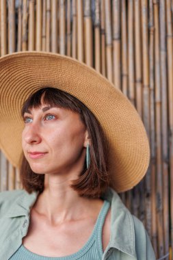 Güzel, gezgin, esmer bir kadının yakın plan portresi. Şapkalı, şık yaz kıyafetleri giyiyor. Yaz tatili boyunca sahilde gülümseyen neşeli genç bir kadın. Mutlu kız.