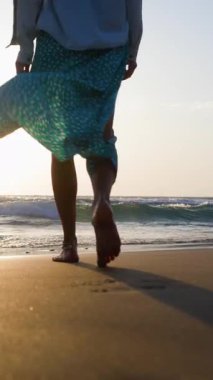 Dikey çekim. Genç ve zayıf bir kadın kumsalda yavaşça yürür ve denize girer. Kumsalda romantik bir atmosfer
