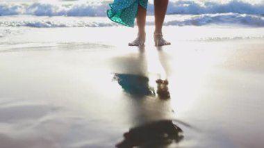 Yaz havası. Suyun yavaş hareketi. Dişi bacaklar yakın plan. Altın gün batımında sahilde duran kız. Yaz tatilindeki turist