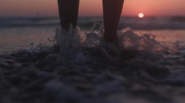 Dişi bacaklar yakın plan. Kumun üzerinde duran ve bacaklarına dokunan bir kız. Sahildeki kız. Yaz tatilindeki turist.