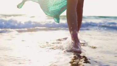 Romantik bir ruh hali. İnce kadın bacakları kumlu sahilde deniz dalgaları boyunca yürüyor. Sörf üzerinde yürüyen güzel bir kadın