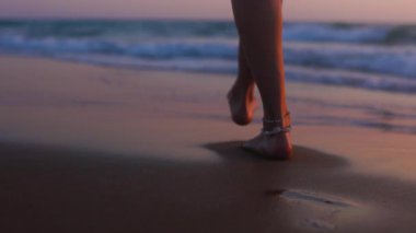 Romantik bir ruh hali. İnce kadın bacakları kumlu sahilde deniz dalgaları boyunca yürüyor. Sörf üzerinde yürüyen güzel bir kadın