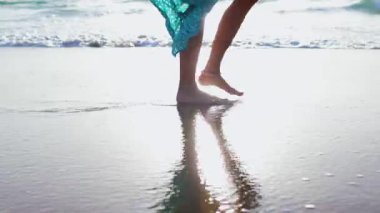 Romantik bir ruh hali. İnce kadın bacakları kumlu sahilde deniz dalgaları boyunca yürüyor. Sörf üzerinde yürüyen güzel bir kadın