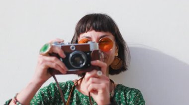 Çekici genç gezgin kadın güneş gözlüğü takıyor ve modern giyim tarzı fotoğraf çekiyor ve kameraya bakıyor.