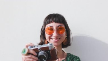 Çekici genç gezgin kadın güneş gözlüğü takıyor ve modern giyim tarzı fotoğraf çekiyor ve kameraya bakıyor.