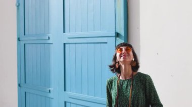 Kafasına güneş gözlüğü takmış çekici bir genç gezgin ve modern tarzda giyinmiş cadde boyunca yürüyor ve fotoğraf çekiyor.