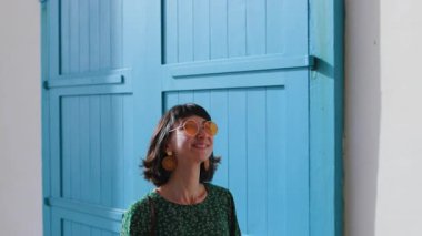 Şık görünümlü güzel bir kadın, şık güneş gözlükleriyle, kendine güvenerek caddede yürüyor. Neşe