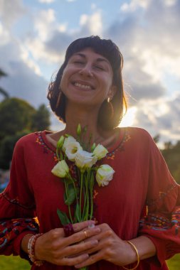 Romantik bir ruh hali. Güzel elbiseli güzel bir kadının portresi ve gün batımında elinde bir buket çiçekle. Kız gülümser ve kameraya bakar..