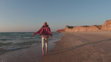 Romantik bir ruh hali. Boş bir sahilde, deniz kıyısında sakince yürüyen genç bir kadın görüntüsü. Tatil ve açık hava eğlencesi.