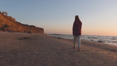 Romantik bir ruh hali. Boş bir sahilde, deniz kıyısında sakince yürüyen genç bir kadın görüntüsü. Tatil ve açık hava eğlencesi.