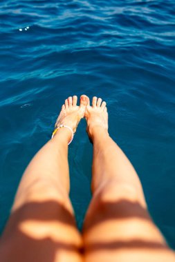 Kız iskelede oturuyor ve ayaklarını denizin mavi ve şeffaf sularına koyuyor. Yaz havası. Güzel ince ve bronzlaşmış bacakları olan bir kadın. Suda dinlenen bir kadın. Ayaklarını suya çarpan bir kadın..