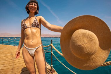 Yaz havası. Bikinili genç, sıska bir kadın denizin kenarında duruyor ve kameraya gülümsüyor. Kız yaz tatilinin tadını çıkarıyor. Kızıl Deniz 'de tatil, Eilat. İsrail.