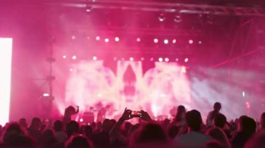 Seyirciler kollarını kaldırmış, yanıp sönen ışıklar ve güçlü bir atmosferi olan enerjik bir kaya gösterisinin keyfini çıkarıyorlar. Kalabalık canlı müzikten hoşlanıyor.