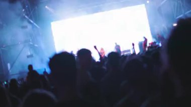 Seyirciler el sallıyor ve sahne ışıkları altında bir rock konserinde video çekiyor. Taraftarlar ellerini havaya kaldırsın, siluetler