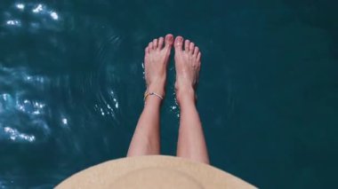 Bikinili bir kadın havuz kenarında ayakları suyun içinde oturuyor. Tropikal tatil, dinlenme ve yaz yaşam tarzı için ideal bir yer.