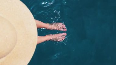 Bikinili bir kadın havuz kenarında ayakları suyun içinde oturuyor. Tropikal tatil, dinlenme ve yaz yaşam tarzı için ideal bir yer.