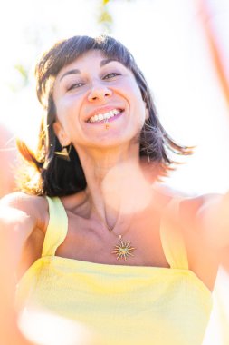 Havalı yaz kıyafetleri içinde, yüzü piercingli, gülümseyen genç bir esmer. Güneşli bir günde dışarıda poz veren baştan çıkarıcı, kaygısız kadın. Açık havada pozitif model. Yaz havası.