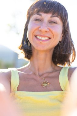 Zarif sarı elbiseli, güzel, gülümseyen esmer kız. Günbatımında dışarıda poz veren baştan çıkarıcı, kaygısız kadın. Güneşli bir günde pozitif bir model. Yaz havası.