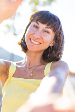 Zarif sarı elbiseli, güzel, gülümseyen esmer kız. Günbatımında dışarıda poz veren baştan çıkarıcı, kaygısız kadın. Güneşli bir günde pozitif bir model. Yaz havası.