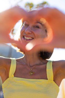 Genç bir kadının ellerinin parmaklarıyla kalp şeklini oluşturması. Güzel genç bir kadının portresi parmaklarıyla kalbi şekillendiriyor ve kameraya bakıyor. Romantik ruh hali.