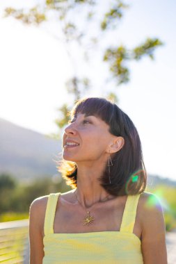 Havalı yaz kıyafetleri içinde, yüzü piercingli, gülümseyen genç bir esmer. Güneşli bir günde dışarıda poz veren baştan çıkarıcı, kaygısız kadın. Açık havada pozitif model. Yaz havası.