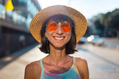 Güneş gözlüğü ve hasır şapkayla kameraya bakan gülümseyen genç bir kadının portresi. Tarz ve moda. Yakın plan..