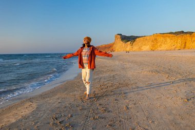 Gülümseyen neşeli kız sahilde eğleniyor anın tadını çıkarıyor. Plajda yürüyen tişörtlü bir kadın. Tatilde bir turist. Seyahat ve macera.