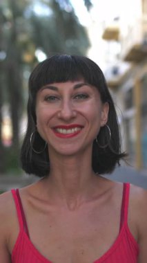 Dikey çekim, kırmızı gece elbisesi giymiş seksi esmer şehir caddesinde kameraya gülümsüyor. Kız portresi. Elbiseli kız.