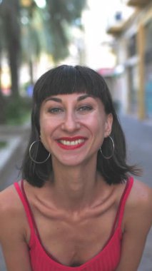 Dikey çekim, kırmızı gece elbisesi içinde seksi esmer kameraya gülümseyen ve şehir caddesinde neşeli bir öpücük yollayan. & Portre