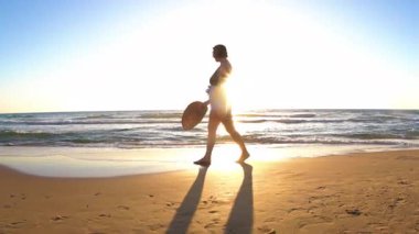 Gün batımında sahilde yürüyen bir kız. Ayrıca plajda ıslak kumda yürüyen ve vücudunun tadını çıkaran bir manken.