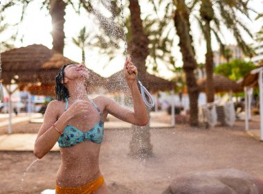 Genç kız tropikal bir duş alıyor. Kumsalda duş al. Kadın vücudunu yıkıyor. Mayo giymiş bir kadının duş alırken görüntüsü. Plajda bikinili bir kız. Yaz havası.