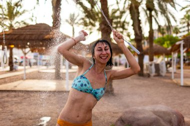 Yaz havası. Güneşli bir günde, plajdaki lüks bir otelde mayo giymiş esmer, beyaz bir kadın ferahlatıcı bir tropikal duş alıyor. Mayolu kız..