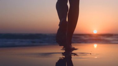 Islak kumda sahilde yürüyen kız. Gün batımında okyanus sahilinde yürüyen bir kadının arka görüntüsü. Ağır çekim. Ağır çekim. Yaz havası.