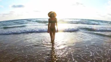 Sahilde sıska bir kadın ve arkasında güzel bir deniz batımı var. Mutlu genç kadın yürürken kendini özgür ve neşeli hissediyor.