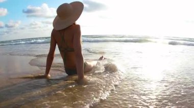 Yaz havası. Kumda oturan ve okyanus dalgalarının tadını çıkaran bir kız. Genç bir kadın kumlu bir sahilde güneşleniyor. Yaz tatili