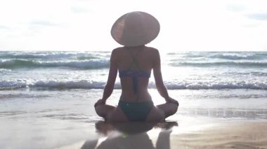 Okyanus kıyısındaki kumlu sahilde meditasyon yapan bir kadın. Arkadan bak. Rahatlama ve canlılığın yenilenmesi, sağlıklı yaşam tarzı...