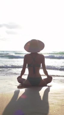 Dikey çekim. Okyanus kıyısındaki kumlu sahilde meditasyon yapan bir kadın. Arkadan bak. Rahatlama ve canlılığın yenilenmesi, sağlıklı